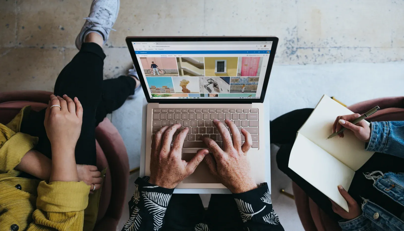 Three persons sitting around each other, one with a laptop, and another with a notebook and pen 