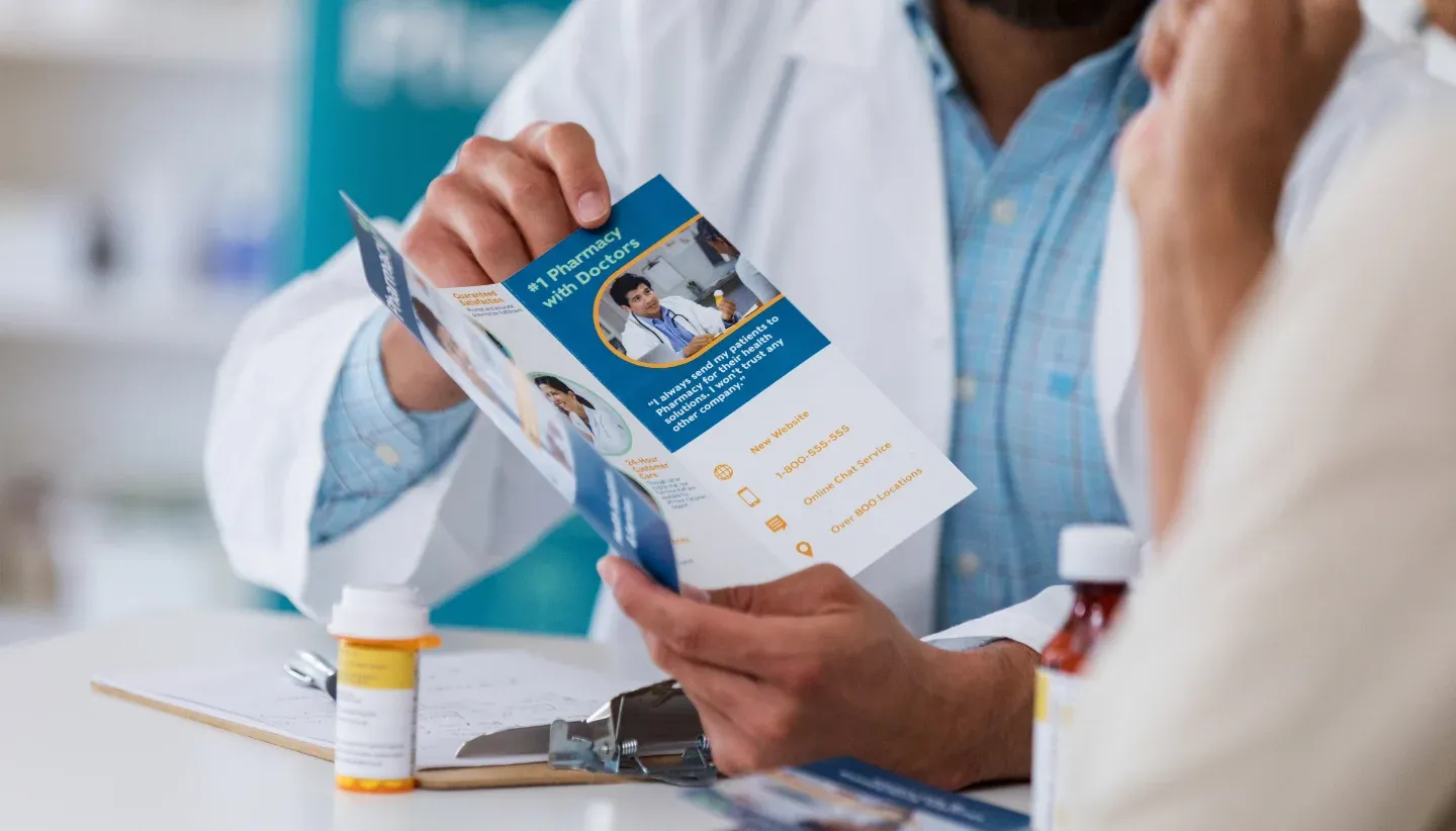 Two healthworkers on a desk, one is holding a flyer about pharmacy
